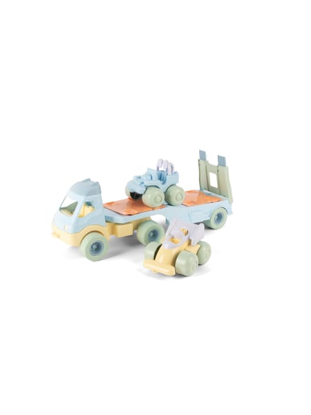 Person i stribet blå skjorte og prikket hat med pastelfarvet legetøj på sandunderlag.